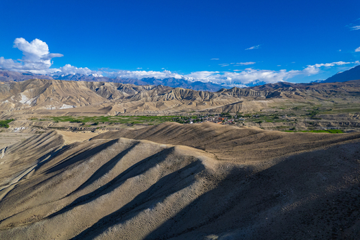 Aerial view of arid mountain ridges and a lush green valley nestled among the Himalayan peaks under a clear blue sky in Nepal.