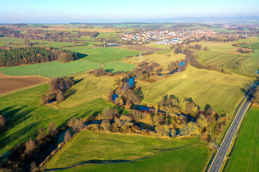 Aerial view of the winding Aisch river flowing through lush green meadows and agricultural fields near a small village in Uehlfeld Bayern Germany. Aerial view of the winding Aisch river flowing through lush green meadows and agricultural fields near a small village in Uehlfeld Bayern Germany.