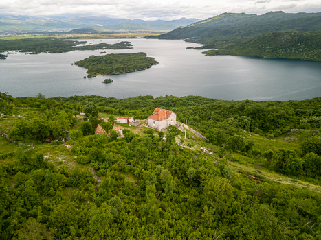 Aerial view of Slansko Lake with a small stone building on a lush green hill surrounded by dense forest and mountains in Niksic Municipality Montenegro. Aerial view of Slansko Lake with a small stone building on a lush green hill surrounded by dense forest and mountains in Niksic Municipality Montenegro.