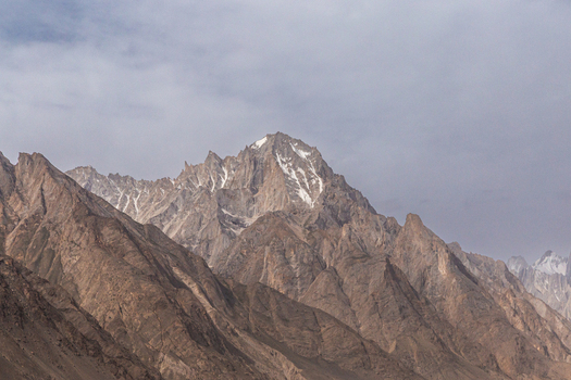 View of the rugged peaks of the Baltoro Glacier with snow dusted rocky slopes under a cloudy sky in Baltoro Gilgit Baltistan Pakistan.