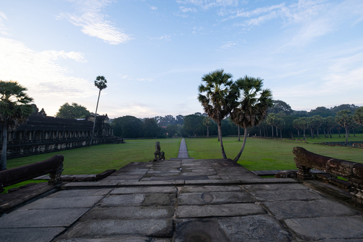 View of the historic Angkor Wat temple grounds with stone pathways palm trees and lush green lawns under a clear blue sky in Krong Siem Reap Siem Reap Province Cambodia.