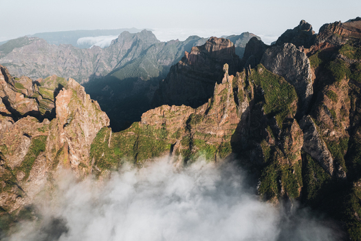 Aerial view of the rugged sun kissed peaks pierce through ethereal clouds creating a dramatic landscape of shadows and light Pico do Areeiro Madeira Portugal.