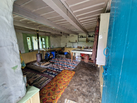 View of the interior of a traditional house featuring a wood burning stove patterned rugs on the floor and a kitchen area in Malana Himachal Pradesh India.