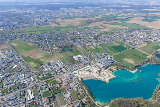 Aerial view of the contrasting turquoise lake against the beige quarry nestled beside the green fields and urban sprawl Sausheim Grand Est France.