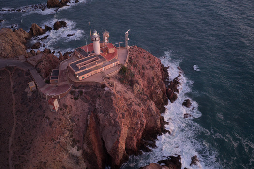 Aerial view of Lighthouse de Cabo de Gata perched on a rugged cliff overlooking the Mediterranean Sea at sunset in San Jose Andalucia Spain. Aerial view of Lighthouse de Cabo de Gata perched on a rugged cliff overlooking the Mediterranean Sea at sunset in San Jose Andalucia Spain.
