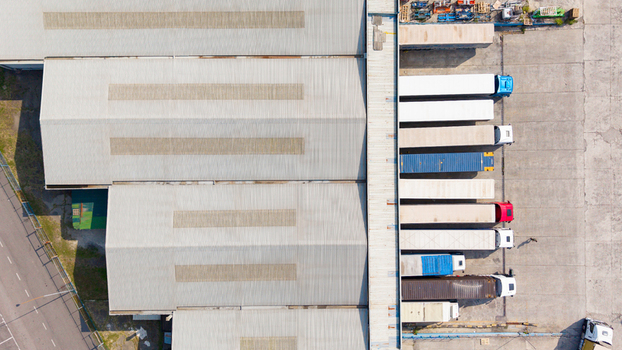 Aerial view of trucks parked at distribution center loading docks with large warehouse roof and concrete yard in San Giuliano Milanese Lombardy Italy. Aerial view of trucks parked at distribution center loading docks with large warehouse roof and concrete yard in San Giuliano Milanese Lombardy Italy.