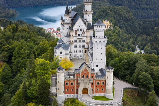 Aerial view of Neuschwanstein Castle rising majestically amidst the dense green forest with a blue lake in the backdrop Neuschwanstein Castle Bayern Germany. Aerial view of Neuschwanstein Castle rising majestically amidst the dense green forest with a blue lake in the backdrop Neuschwanstein Castle Bayern Germany.