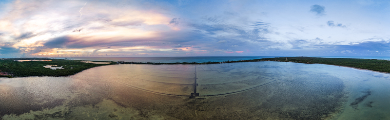 Aerial view of Salt Pond featuring grid like salt pans surrounded by lush green vegetation and the ocean under a sunset sky in Exuma Exuma The Bahamas.