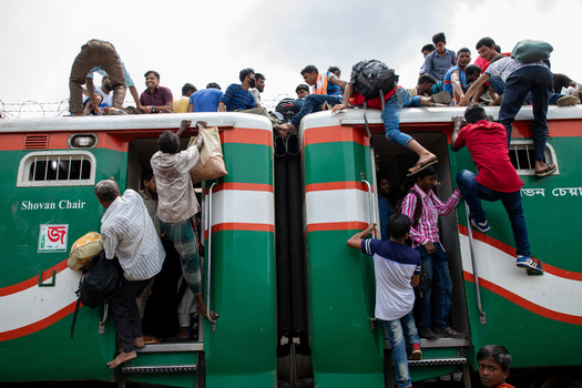Dhaka Bangladesh 14 June 2018 View of crowds of people climbing onto the roof and hanging from the doors of a green and red passenger train at Airport Railway Station. Dhaka Bangladesh 14 June 2018 View of crowds of people climbing onto the roof and hanging from the doors of a green and red passenger train at Airport Railway Station.