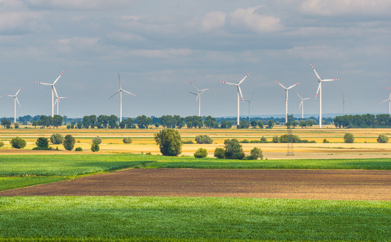 Aerial view of a wind farm with multiple wind turbines standing in agricultural fields with green and brown crops under a cloudy sky in Tczew Pomeranian Voivodeship Poland. Aerial view of a wind farm with multiple wind turbines standing in agricultural fields with green and brown crops under a cloudy sky in Tczew Pomeranian Voivodeship Poland.