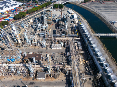 Aerial view of an industrial oil refinery complex with tall processing towers storage tanks and cooling fans situated next to a waterway in Carson California United States.