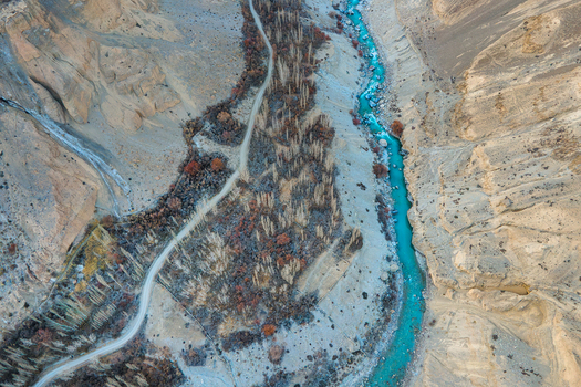 Aerial view of a turquoise river snaking through a stark rocky valley flanked by autumn tinged trees and winding paths Hunza Nagar Gilgit Pakistan. Aerial view of a turquoise river snaking through a stark rocky valley flanked by autumn tinged trees and winding paths Hunza Nagar Gilgit Pakistan.