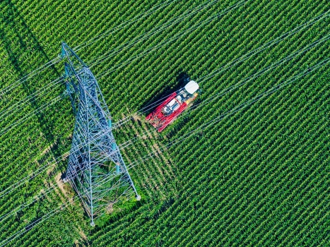 Aerial view of a tractor working in a green field next to a large electricity pylon in Hombourg Grand Est France. Aerial view of a tractor working in a green field next to a large electricity pylon in Hombourg Grand Est France.