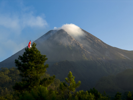 Aerial view of Mount Merapi volcano with smoke at the summit and lush pine trees in the foreground Kecamatan Pakem Daerah Istimewa Yogyakarta Indonesia. Aerial view of Mount Merapi volcano with smoke at the summit and lush pine trees in the foreground Kecamatan Pakem Daerah Istimewa Yogyakarta Indonesia.