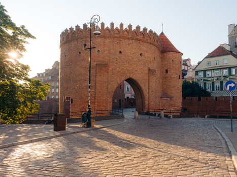 View of the historic red brick Warsaw Barbican fortification with cobblestone streets and warm golden hour light in Warsaw Masovian Voivodeship Poland. View of the historic red brick Warsaw Barbican fortification with cobblestone streets and warm golden hour light in Warsaw Masovian Voivodeship Poland.