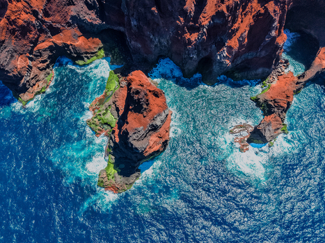 Aerial view of rugged rust colored cliffs meet the turquoise sea creating a striking contrast of textures and tones Capelo A&ccedil;ores Portugal.