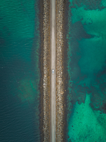 Aerial view of a lone white car traverses the Flakstadbruene bridge amidst the stunning turquoise waters of the Norwegian Sea Flakstadbruene Nordland Norway. Aerial view of a lone white car traverses the Flakstadbruene bridge amidst the stunning turquoise waters of the Norwegian Sea Flakstadbruene Nordland Norway.