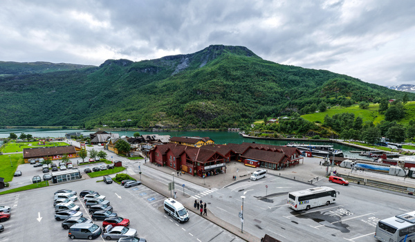 Aerial view of the village of Flam featuring the harbor red wooden buildings a parking area with buses and cars and lush green mountains in Flam Vestland Norway. Aerial view of the village of Flam featuring the harbor red wooden buildings a parking area with buses and cars and lush green mountains in Flam Vestland Norway.