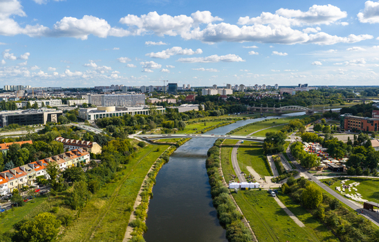 Aerial view of the Warta river flowing through the city with green riverbanks a bridge and urban buildings under a blue sky in Poznan Greater Poland Voivod Poland.