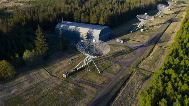 Aerial view of the Westerbork Synthesis Radio Telescope dishes and a large hangar building surrounded by dense green forest and open fields Zwiggelte Drenthe Netherlands. Aerial view of the Westerbork Synthesis Radio Telescope dishes and a large hangar building surrounded by dense green forest and open fields Zwiggelte Drenthe Netherlands.