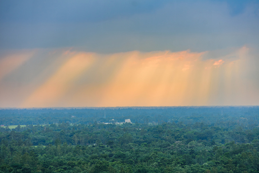 Aerial view of dramatic sunbeams breaking through dark storm clouds over a vast expanse of lush green forest in Bogura Rajshahi Division Bangladesh. Aerial view of dramatic sunbeams breaking through dark storm clouds over a vast expanse of lush green forest in Bogura Rajshahi Division Bangladesh.