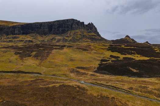 Aerial view of The Quiraing landslip featuring dramatic rock formations and a winding road with a lone car under a cloudy sky Isle of Skye Scotland United Kingdom. Aerial view of The Quiraing landslip featuring dramatic rock formations and a winding road with a lone car under a cloudy sky Isle of Skye Scotland United Kingdom.