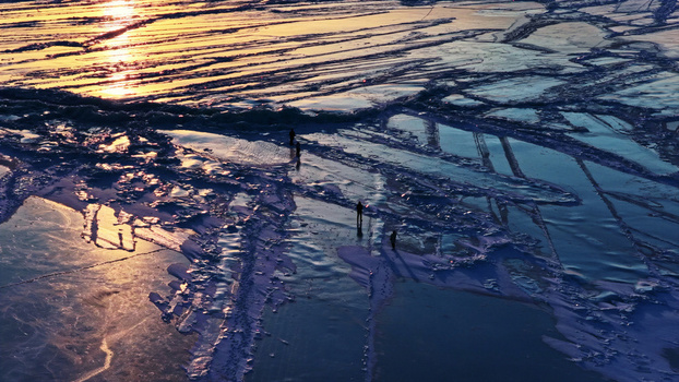 Aerial view of people walking on the cracked ice of a frozen lake during golden hour in Latvia. Aerial view of people walking on the cracked ice of a frozen lake during golden hour in Latvia.