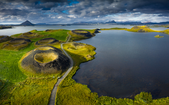 Aerial view of the Skutustadagigar pseudocraters and lush green hills along the shores of Lake Myvatn under a dramatic cloudy sky Iceland.