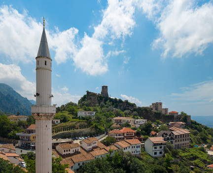 Aerial view of the historic Kruje Castle and a tall white minaret overlooking traditional red tiled rooftops and lush green hills under a blue sky in Kruje Durres County Albania.