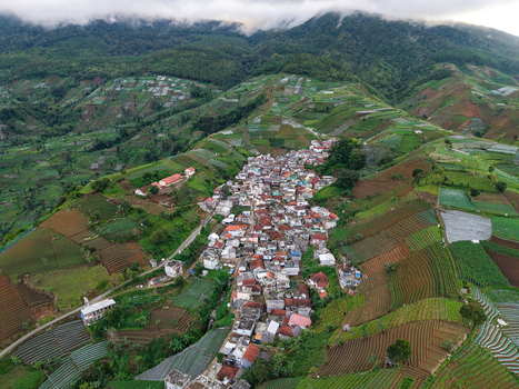 Aerial view of Terasering Panyaweuyan with its lush green terraced fields surrounding a village with red roofed houses in the mountains of Kecamatan Argapura Jawa Barat Indonesia. Aerial view of Terasering Panyaweuyan with its lush green terraced fields surrounding a village with red roofed houses in the mountains of Kecamatan Argapura Jawa Barat Indonesia.