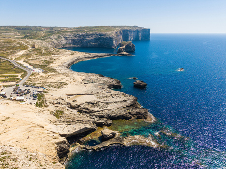 Aerial view of the rugged limestone cliffs and turquoise waters of Dwejra Bay under a clear blue sky in Gozo Region Malta. Aerial view of the rugged limestone cliffs and turquoise waters of Dwejra Bay under a clear blue sky in Gozo Region Malta.