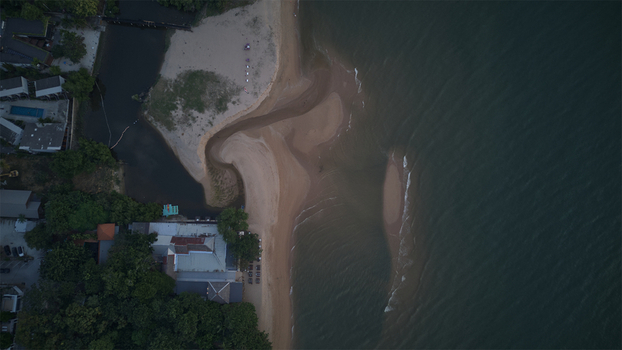 Aerial view of Jomtien Beach featuring the sandy shoreline meeting the dark sea water alongside coastal buildings and lush green trees in Chon Buri Thailand.