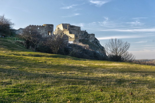 View of the ancient stone ruins of Devin Castle on a rocky hill overlooking a grassy meadow and bare trees under a clear blue sky in Bratislava IV Bratislava Region Slovakia. View of the ancient stone ruins of Devin Castle on a rocky hill overlooking a grassy meadow and bare trees under a clear blue sky in Bratislava IV Bratislava Region Slovakia.