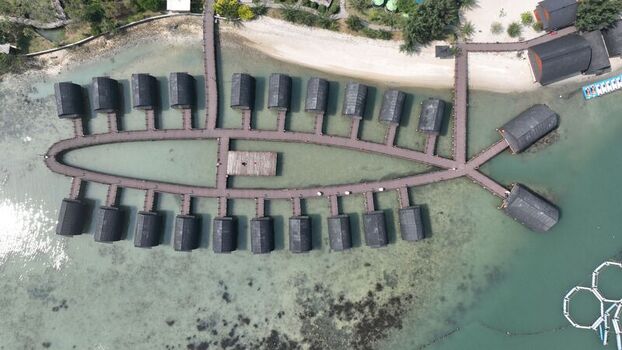 Aerial view of Pulau Lima Resort featuring a unique fish shaped wooden walkway with overwater huts surrounded by clear shallow water in Kasemen Banten Indonesia. Aerial view of Pulau Lima Resort featuring a unique fish shaped wooden walkway with overwater huts surrounded by clear shallow water in Kasemen Banten Indonesia.