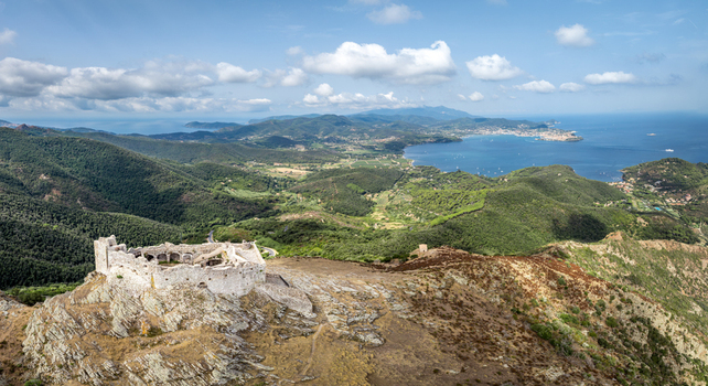 Aerial view of Castello del Volterraio perched on a rocky hill overlooking the lush green landscape and the blue bay of Portoferraio Toscana Italy.