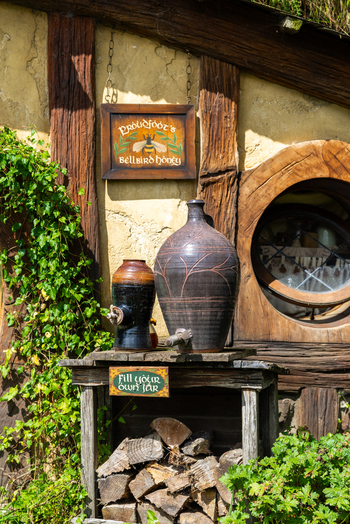 View of rustic charm with stacked firewood earthenware jugs and climbing ivy against a Hobbit hole Hobbiton Movie Set Waikato Region New Zealand. View of rustic charm with stacked firewood earthenware jugs and climbing ivy against a Hobbit hole Hobbiton Movie Set Waikato Region New Zealand.