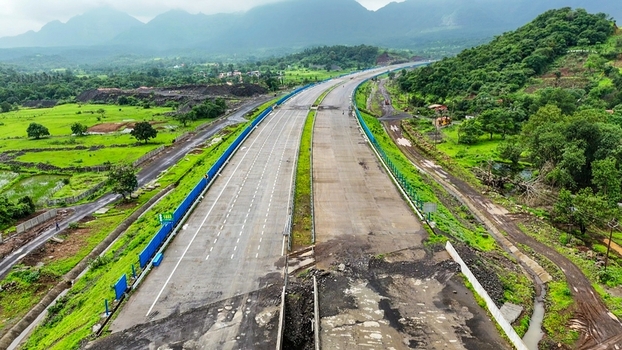 Aerial view of the Delhi Mumbai Expressway cutting through a lush green landscape with rolling hills in the background in Badlapur Maharashtra India. Aerial view of the Delhi Mumbai Expressway cutting through a lush green landscape with rolling hills in the background in Badlapur Maharashtra India.