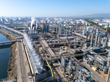 Aerial view of an industrial oil refinery complex featuring cooling towers with rising steam extensive pipe networks and storage tanks located in Carson California United States.