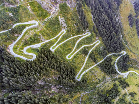 Aerial view of the winding Silvretta Hochalpenstrasse mountain road with sharp hairpin turns cutting through dense coniferous forests and alpine slopes in Partenen Vorarlberg Austria. Aerial view of the winding Silvretta Hochalpenstrasse mountain road with sharp hairpin turns cutting through dense coniferous forests and alpine slopes in Partenen Vorarlberg Austria.
