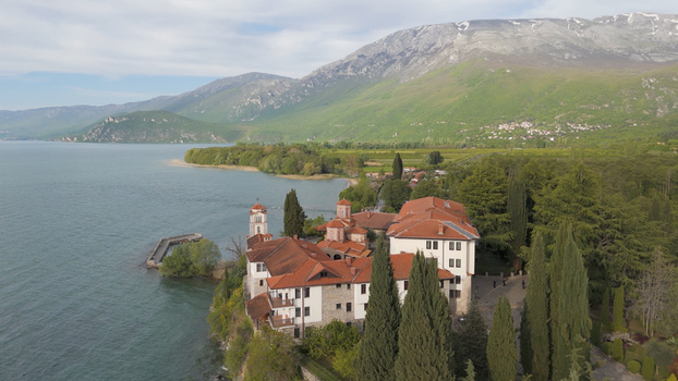 Aerial view of Saint Naum Monastery situated on the shore of Lake Ohrid with red tiled roofs stone walls lush trees and mountains in the background in Municipality of Ohrid North Macedonia.