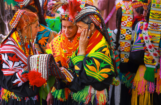 Chitral Khyber Pakhtunkhwa Pakistan 12 June 2015 View of Kalash women in traditional colorful embroidered clothing and headpieces interacting during a cultural gathering in Rumbur.