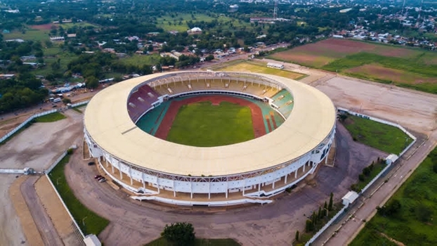 Aerial view of a large circular stadium with a green pitch and running track surrounded by open land and sparse buildings Ghana. Aerial view of a large circular stadium with a green pitch and running track surrounded by open land and sparse buildings Ghana.