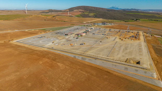 Aerial view of a large electrical substation under construction surrounded by rolling hills and wind turbines in Swellendam Western Cape South Africa. Aerial view of a large electrical substation under construction surrounded by rolling hills and wind turbines in Swellendam Western Cape South Africa.