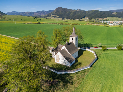 Aerial view of the historic All Saints Church surrounded by lush green fields and rolling hills under a clear blue sky in Ludrova Zilina Region Slovakia. Aerial view of the historic All Saints Church surrounded by lush green fields and rolling hills under a clear blue sky in Ludrova Zilina Region Slovakia.