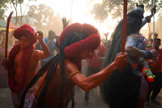 Munshiganj Bangladesh 13 April 2025 View of vibrant figures adorned in striking red headpieces and body paint moving through a hazy sunlit atmosphere showcasing rich cultural traditions. Munshiganj Bangladesh 13 April 2025 View of vibrant figures adorned in striking red headpieces and body paint moving through a hazy sunlit atmosphere showcasing rich cultural traditions.