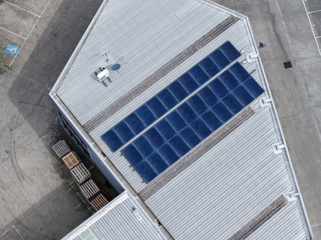 Aerial view of solar panels installed on a corrugated metal roof of an industrial building with wooden pallets on the ground in Melbourne VIC Australia.
