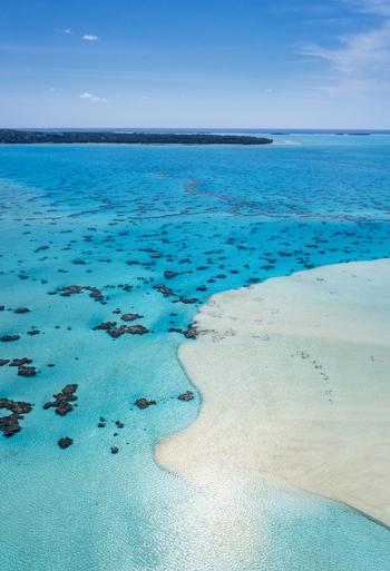 Aerial view of the turquoise Aitutaki lagoon featuring a white sandbar and scattered coral reefs under a clear blue sky in Aitutaki Cook Islands. Aerial view of the turquoise Aitutaki lagoon featuring a white sandbar and scattered coral reefs under a clear blue sky in Aitutaki Cook Islands.