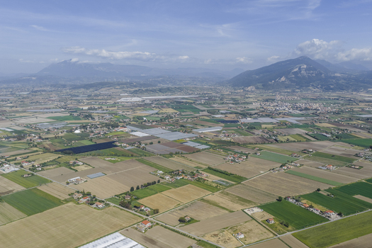 Aerial view of the vast agricultural landscape with a patchwork of green and brown fields greenhouses and distant mountains under a clear sky in Paestum Campania Italy.