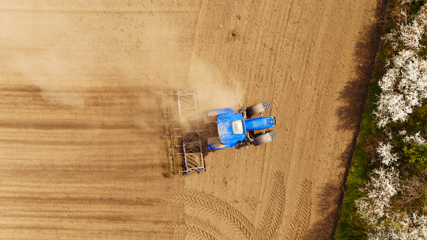 Aerial view of a blue tractor working the brown soil with white blossoming trees lining the field s edge Sremska Mitrovica Vojvodina Serbia. Aerial view of a blue tractor working the brown soil with white blossoming trees lining the field s edge Sremska Mitrovica Vojvodina Serbia.