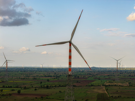 Aerial view of wind turbines with orange and white blades standing in a vast rural landscape with green fields and scattered trees in Hampi Karnataka India.